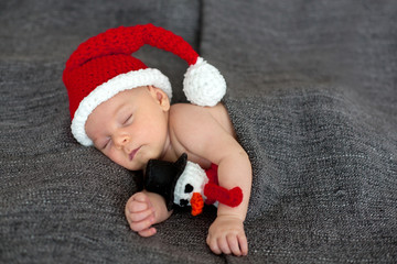 Little sleeping newborn baby boy, wearing Santa hat and holding toy
