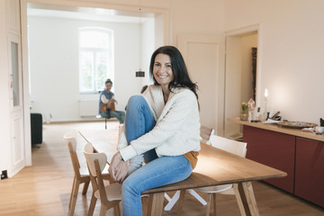 Portrait of smiling woman sitting on table at home