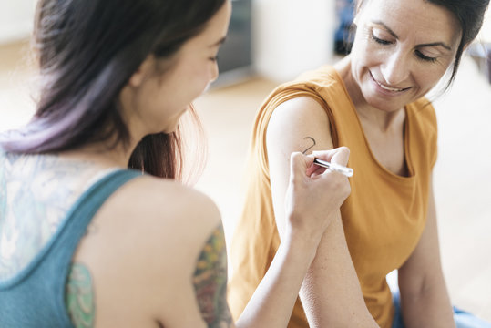 Woman painting tattoo on arm of another woman