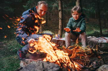 Father with son makes campfire in forest