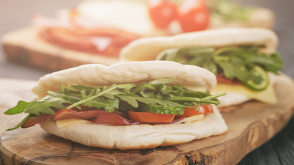 rustic sandwiches with ham arugula and tomatoes in pita bread, on wood table
