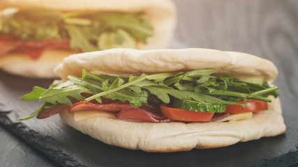 rustic sandwiches with ham arugula and tomatoes in pita bread, on wood table