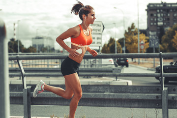 Female runner jogging on the city street by the traffic road.City environment. - obrazy, fototapety, plakaty