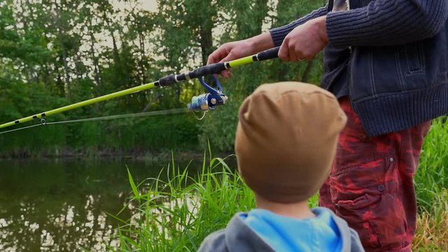 Close up of happy excited child and his father with fishing rod reeling at the river