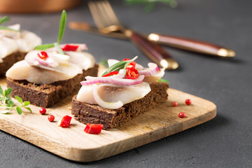 Sandwich with herring, black bread, black background, hot pepper, pickled onion, horizontal, selective focus