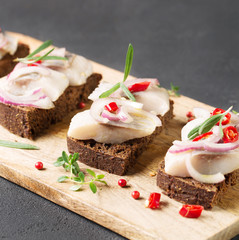 Sandwich with herring, black bread, black background, hot pepper, pickled onion, square, selective focus