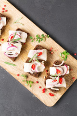 Sandwich with herring, black bread, black background, hot pepper, pickled onion, vertical, top view