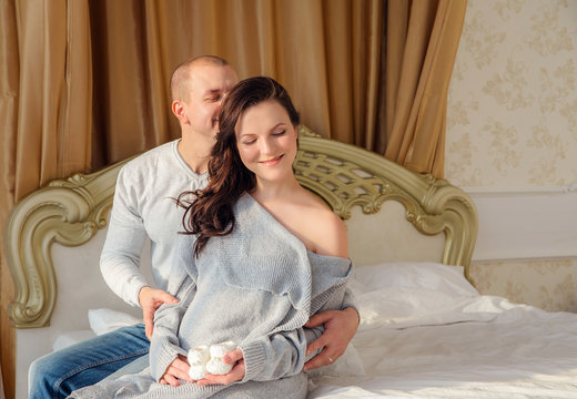 Pregnant woman and husband are smiling spending time together in bed men touching tommy