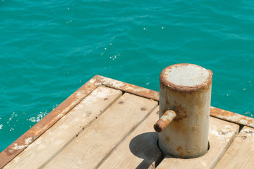 Naklejka premium Old, rusty bollard with metal chain on pier with water