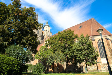 The gothic style Nikolaikirche (Saint Nicholas church) in historical center of Jueterbog, Brandenburg, Germany in a sunny day with blue sky and surrounding park with trees.  Horizontal frame.