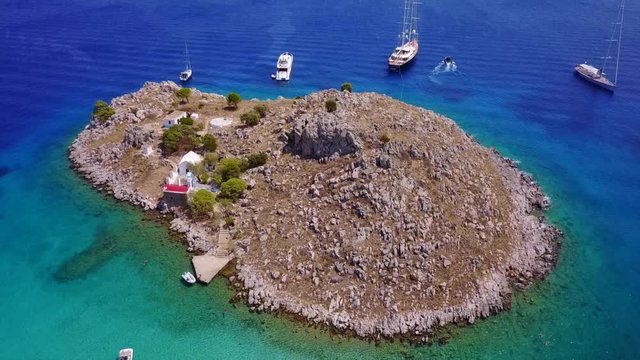 August 2017: Aerial drone video of small heart shaped island with picturesque church of Agia Marina and turquoise clear waters, Symi island, Dodecanese, Aegean, Greece