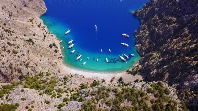 August 2017: Aerial drone video of iconic rocky bay and famous beach of Agios Georgios with turquoise clear waters and boats docked, Symi island, Dodecanese, Aegean, Greece