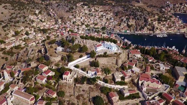 August 2017: Aerial drone video of picturesque castle in Ano chora in island of Symi with traditional architecture and dominant colors, Dodecanese, Aegean, Greece