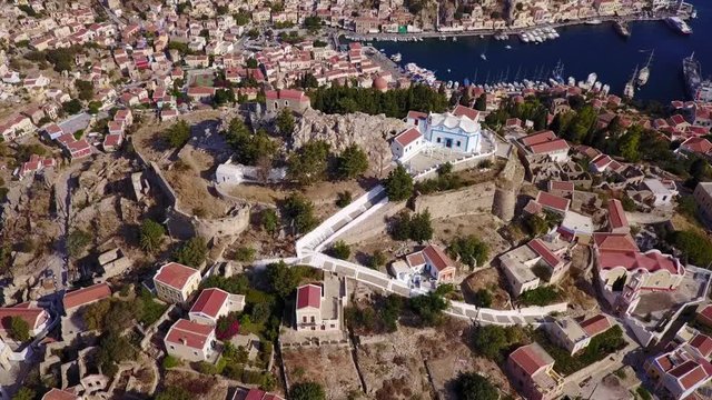 August 2017: Aerial drone video of picturesque castle in Ano chora in island of Symi with traditional architecture and dominant colors, Dodecanese, Aegean, Greece