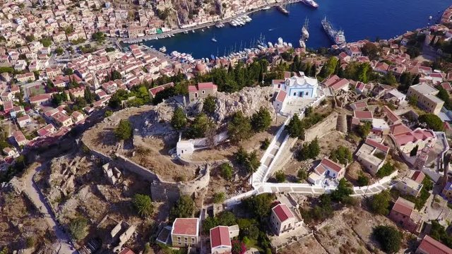 August 2017: Aerial drone video of picturesque castle in Ano chora in island of Symi with traditional architecture and dominant colors, Dodecanese, Aegean, Greece