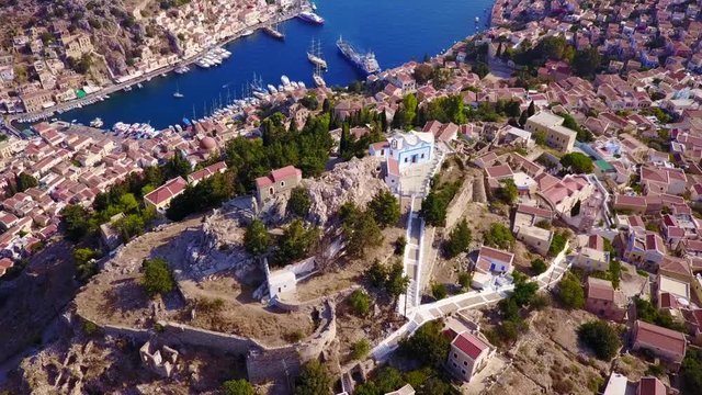 August 2017: Aerial drone video of picturesque castle in Ano chora in island of Symi with traditional architecture and dominant colors, Dodecanese, Aegean, Greece