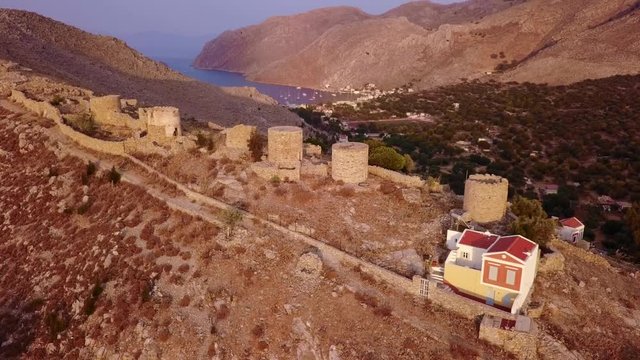 August 2017: Aerial drone video of picturesque old windmills overlooking port of Symi with traditional architecture and dominant colors, Symi island, Dodecanese, Aegean, Greece