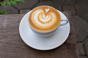 A white cup of coffee latte art on wood table