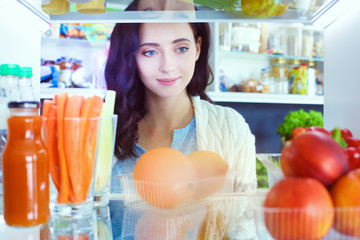 Portrait of female standing near open fridge full of healthy food, vegetables and fruits. Portrait of female