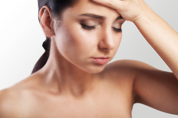 Naklejka premium Portrait of a beautiful young brunette with bare shoulders, severe headaches, migraine, colds. The concept of treatment. Holds his hand to his forehead.