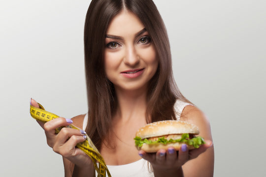 Harmful food. A young girl is struggling with overweight and malicious food. The choice between pohudannam and burger. The concept of health and beauty. On a gray background.