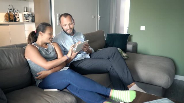 Father with his daughter talking and using tablet on sofa at home
