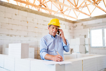 Senior architect with smartphone at the construction site.