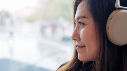 Closeup image of a beautiful Asian woman enjoy listening to music with headphone in modern cafe with feeling relax and happy