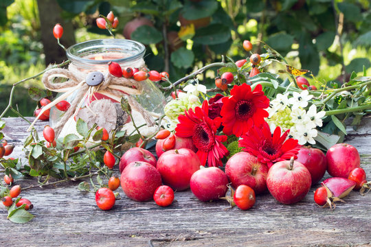 Hagebutten,Herbstblumen,rote &Auml;pfel als Herbstdekoration rustikal auf Holz