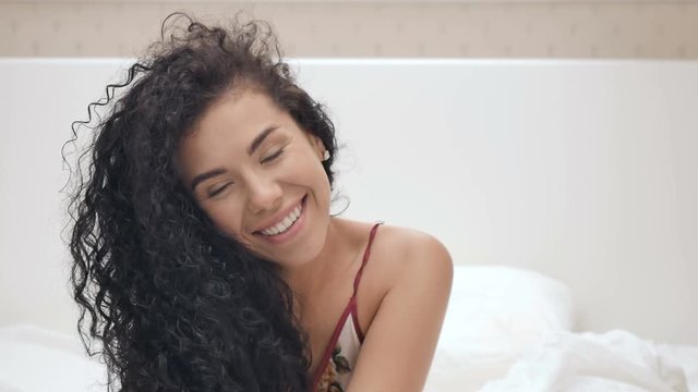 Cute curly brunette poses for camera in white bed