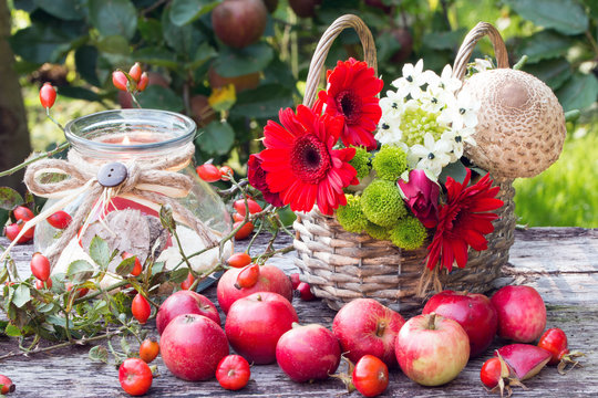 Herbstdekoration mit roten &Auml;pfeln,Herbstblumen im Weidenkorb und Kerze im Glas