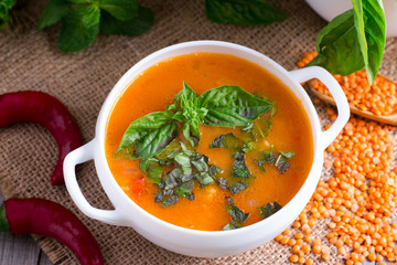 Lentil soup with basil in a ceramic white bowl on a wooden background