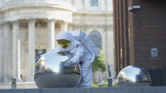  Funny astronaut returned to earth, embracing metal sphere sculpture in city