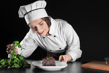 Female chef decorating dessert on dark background