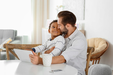 Happy father with adopted African-American boy using tablet computer at home