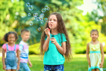Cute little girl blowing soap bubbles outdoors
