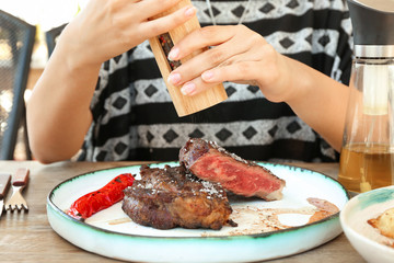 Woman adding salt to steak in restaurant