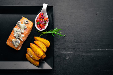 Baked salmon with mushroom sauce and potatoes. On a wooden background. Top view. Free space.