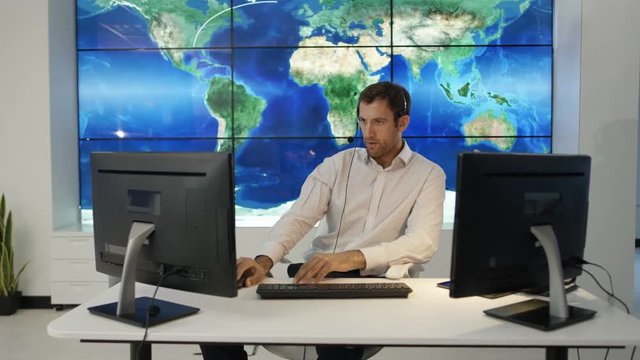  Businessman having conversation via headset with large world map graphic on video wall. Could be global business service agent or airport traffic control room