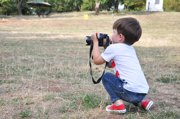 Four years old boy taking photos with camera. Little photographer with professional dslr camera