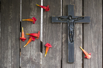 Black wooden crucifix on the shabby wooden  plank with red flowers.