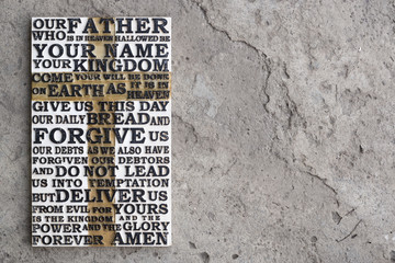 Wooden carved word of the Lord's Prayer on the grey concrete background.
