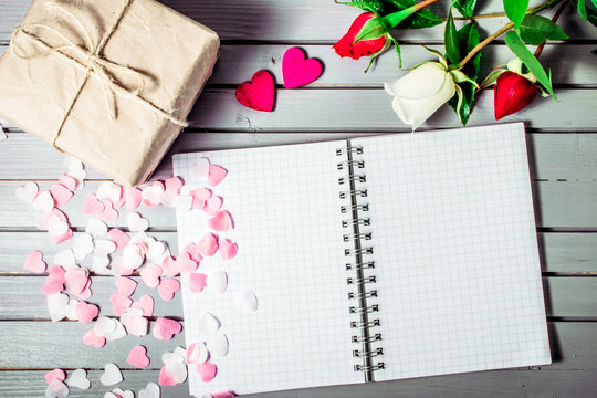 rose flowers close-up with gift box, hearts and blank note book on wooden background. Spring summer border template. mockup floral background. sale, greeting and celebration card concept.