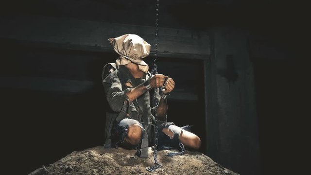 a prisoner in chains is closed in the basement where a little light penetrates