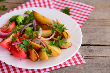 Potato wedges, cooked broccoli, fresh tomato slices with spices, red onion, green parsley leaves on a white plate and on an vintage wooden background. Vegetarian main dish recipe