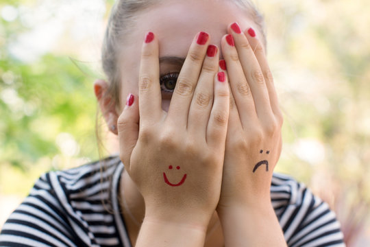 Teenage girl with a smiley and a frown drawn on her hands