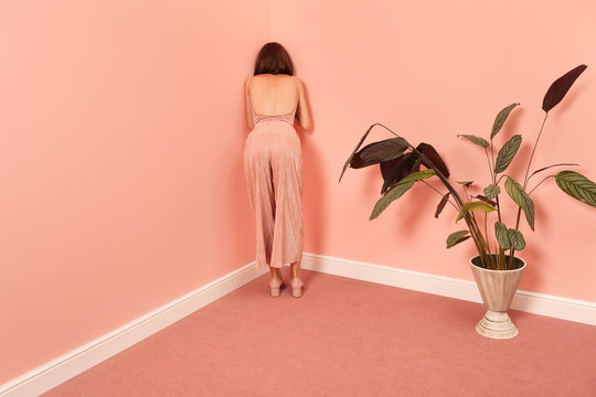 fashionable woman leaning against a pink wall