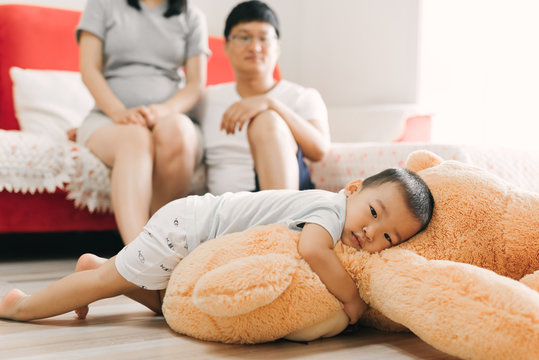 Cute toddler lying on his big Teddy with his parents in the background