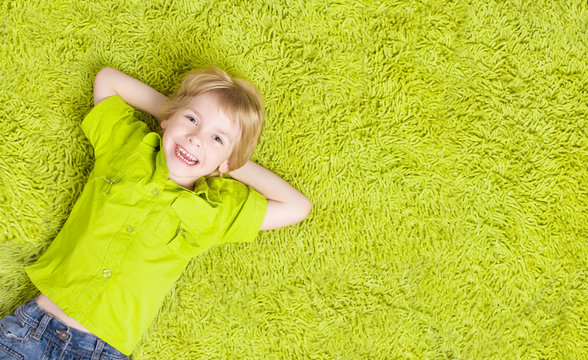 Child Lying Over Green Carpet. Happy Smiling Kid, Boy Five Years Old, Top View