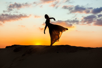 Obraz premium Female dancer dances at sunset, her dress is fluttering and translucent. The backlight of the sun only contours of the figures are visible.